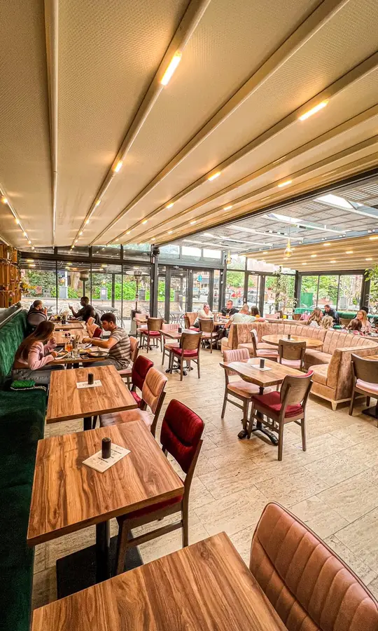 The long dining room, with wooden tables, red velvet chairs and green and pink banquettes